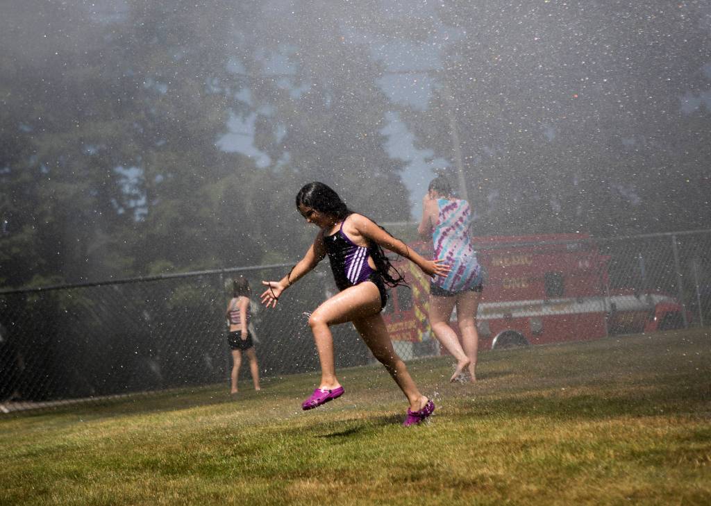Mariam Helali, 9, runs through the fire hose sprinkler station Saturday at Walter E. Hall Park in Everett. (Olivia Vanni / The Herald)
