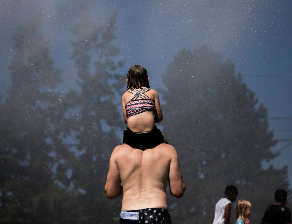 People stand in the spray from the Everett Fire Departments fire hose sprinkler station Saturday at Walter E. Hall Park in Everett. (Olivia Vanni / The Herald)