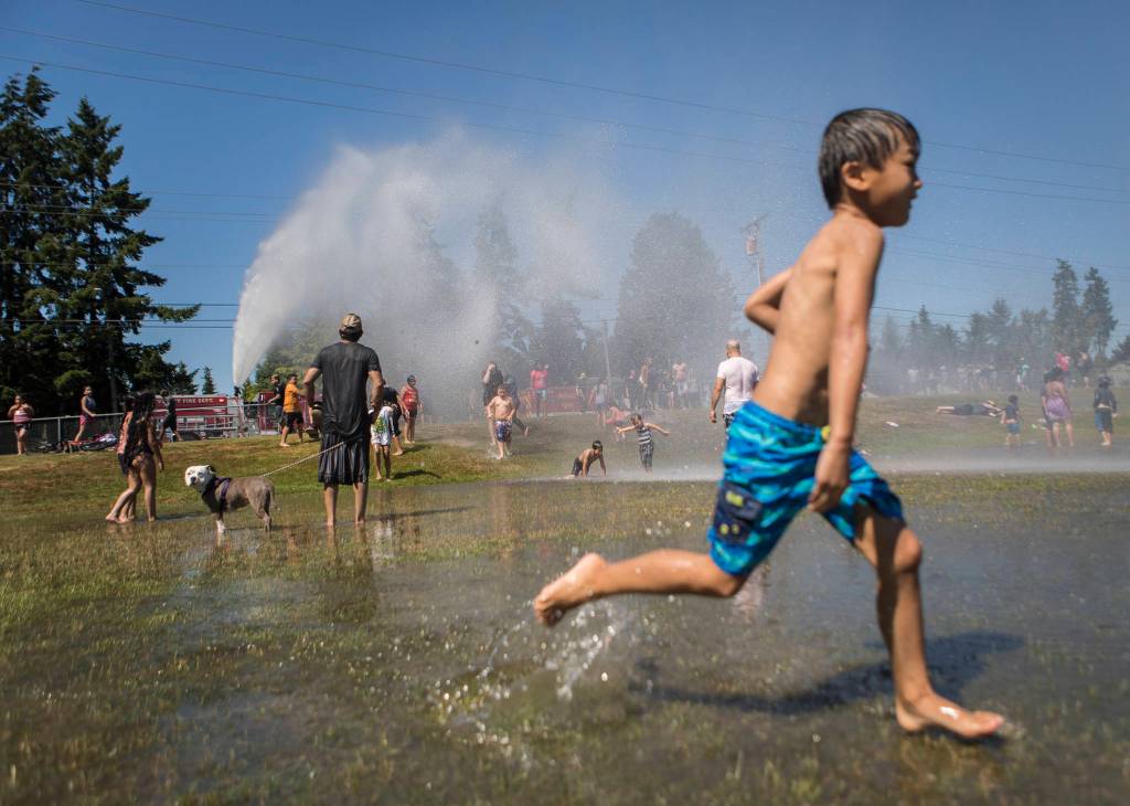People enjoy the fire hose sprinkler station set up Saturday by the Everett Fire Department at Walter E. Hall Park in Everett. (Olivia Vanni / The Herald)