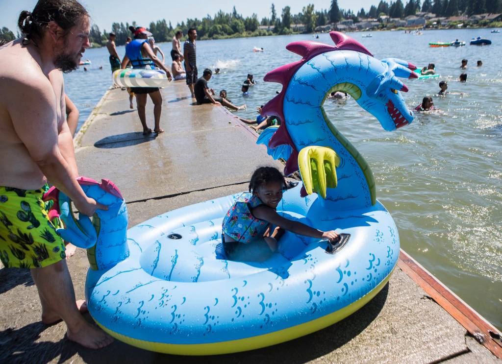 Derick Bradford pushes his son Warren, 5, into the water on his inflatable dragon Saturday at Thornton A. Sullivan Park in Everett. (Olivia Vanni / The Herald)