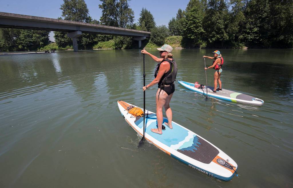 Susan Lange (left) and Debbie Thulen set off on inflatable paddle boards for a trip down the Stillaguamish River during record-setting heat on Monday in Arlington. (Andy Bronson / The Herald)