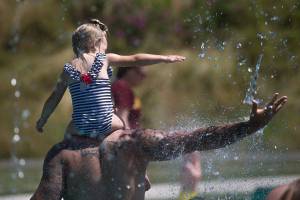 Keeping cool in record setting temperatures, Beau Jess and daughter River, 3, reach for falling water as they play at the Splash Pad in Haller Park on Monday, June 28, 2021 in Arlington, Washington. (Andy Bronson / The Herald)