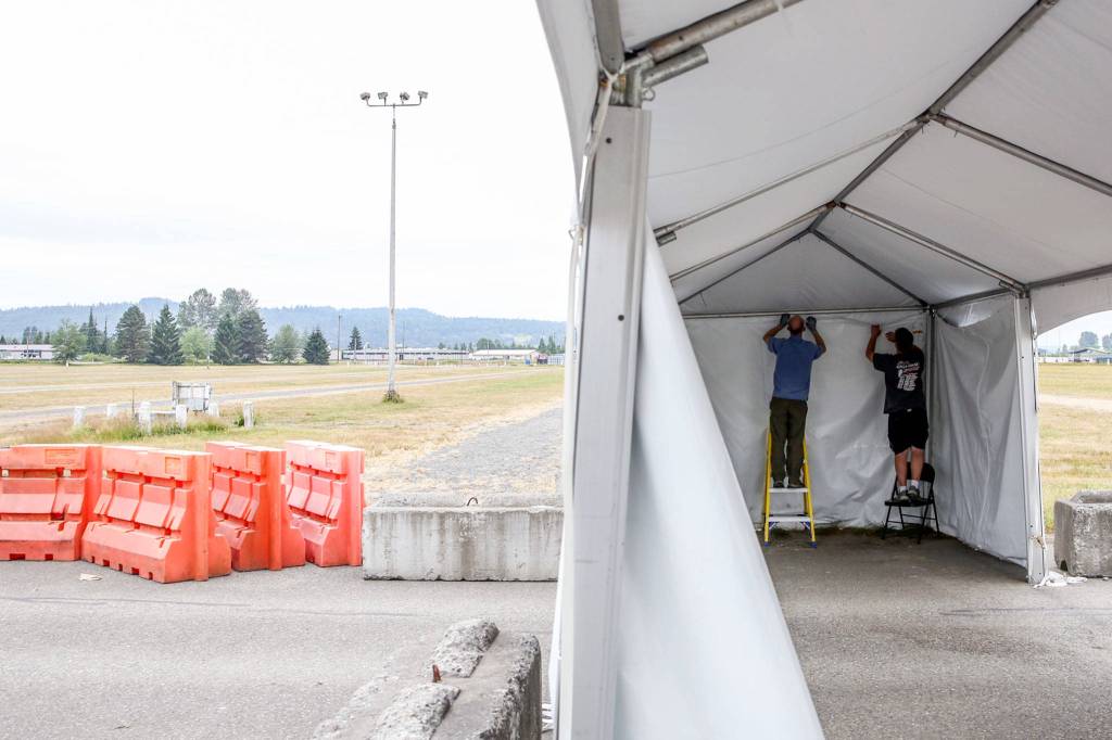 Jeff Irtter (left) and Tom Glasenapp dismantle a tent at the COVID vaccination station at the Evergreen State Fairgrounds in Monroe. (Kevin Clark / The Herald)