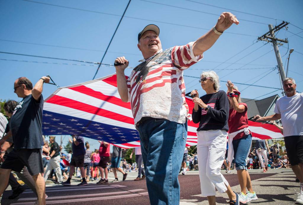 Community members walk down Walnut Street with a large American flag during the Edmonds Kind of 4th parade on Sunday in Edmonds. (Olivia Vanni / The Herald)