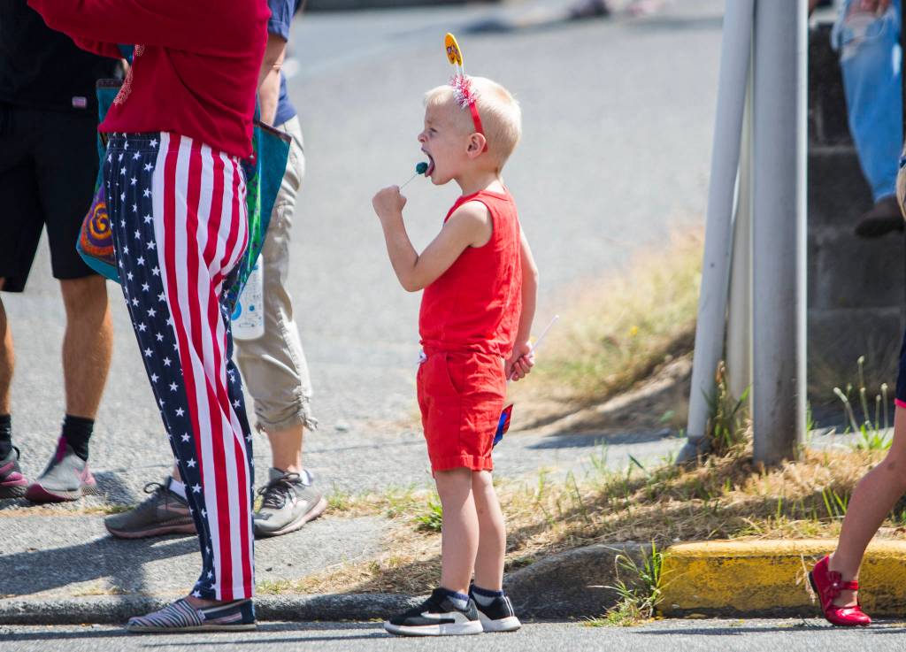 Aksel Young, 3, eats a lollipop while waiting for the Edmonds Kind of 4th parade on Sunday in Edmonds. (Olivia Vanni / The Herald)