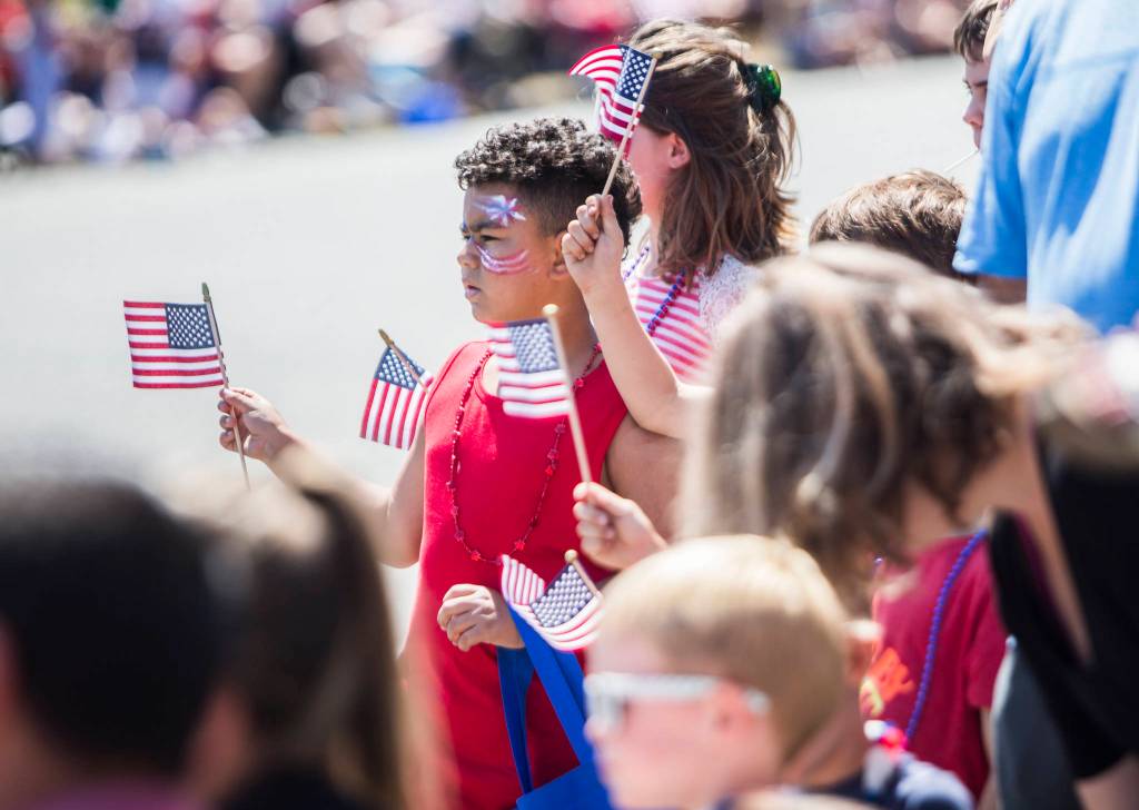 Children wave flags as floats go by during the Edmonds Kind of 4th parade on Sunday in Edmonds. (Olivia Vanni / The Herald)