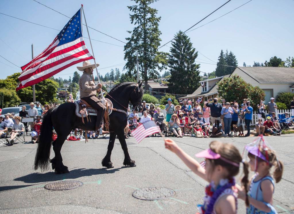 People watch as horses make their way down Sixth Avenue South during the Edmonds Kind of 4th parade on Sunday in Edmonds. (Olivia Vanni / The Herald)