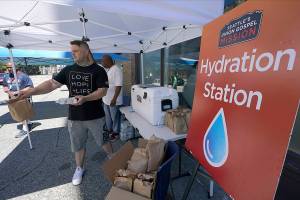 Carlos Ramos hands out bottles of water and sack lunches, Monday, June 28, 2021, as he works at a hydration station in front of the Union Gospel Mission in Seattle. Seattle and other cities broke all-time heat records over the weekend, with temperatures soaring well above 100 degrees Fahrenheit (37.8 Celsius). (AP Photo/Ted S. Warren)