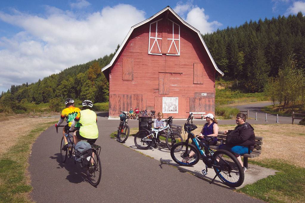 Riders on a tandem bike pass by others enjoying a break at the Nakashima Barn at the north end of the Centennial Trail. (Andy Bronson / The Herald)