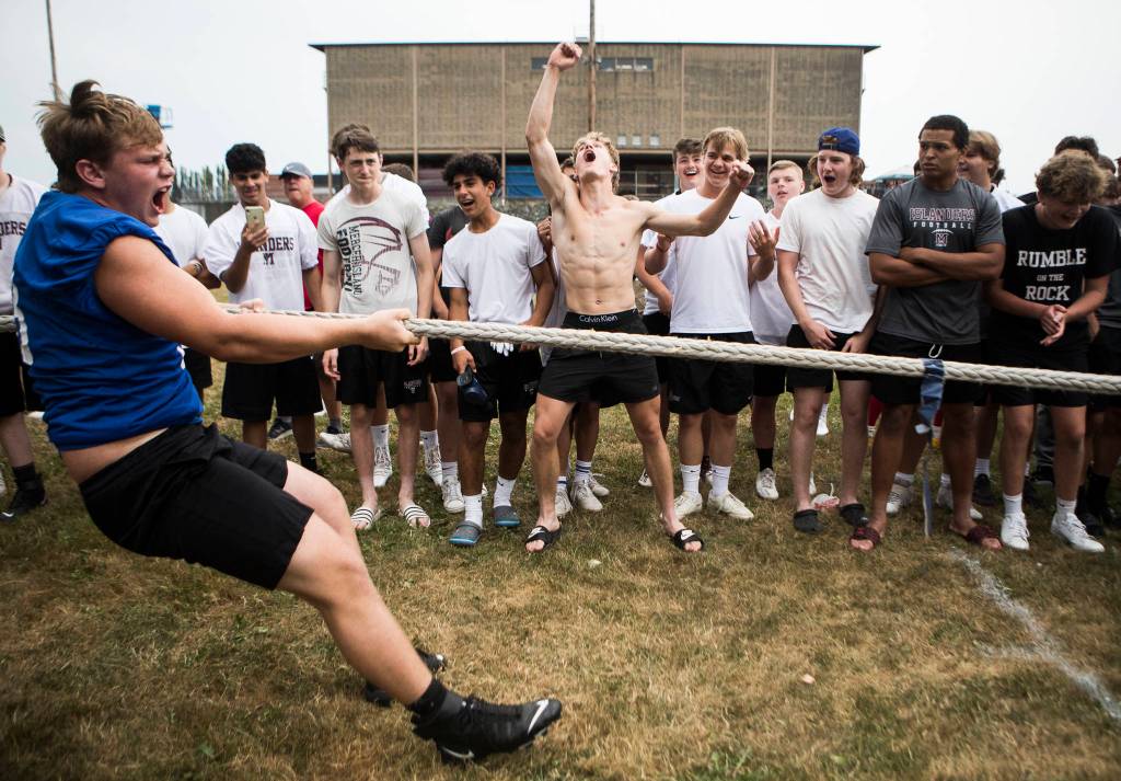 Bothells Luka Vincic (left) yells as he pulls the blue flag across the center to win while Mercer Islands Cole Drayton (center) jumps in celebration during the Cougars Championship Lineman Challenge at Lakewood High School on July 31 in Arlington. (Olivia Vanni / The Herald)