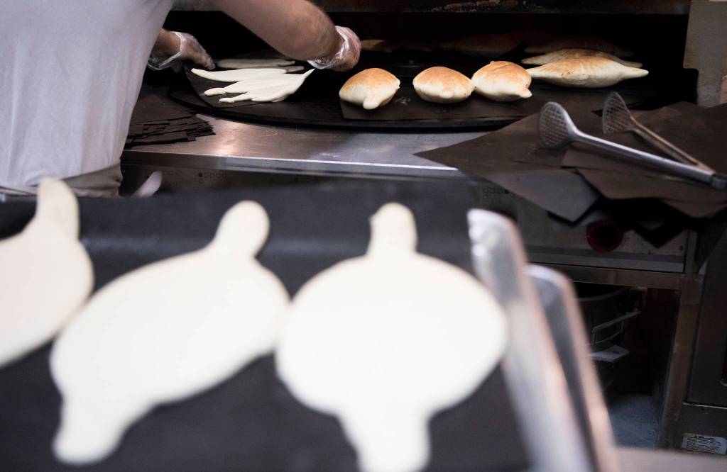 Nechirvan Zebari places pita dough on a rotating plate in a large oven at Alidas Bakery in Everett. (Olivia Vanni / The Herald)