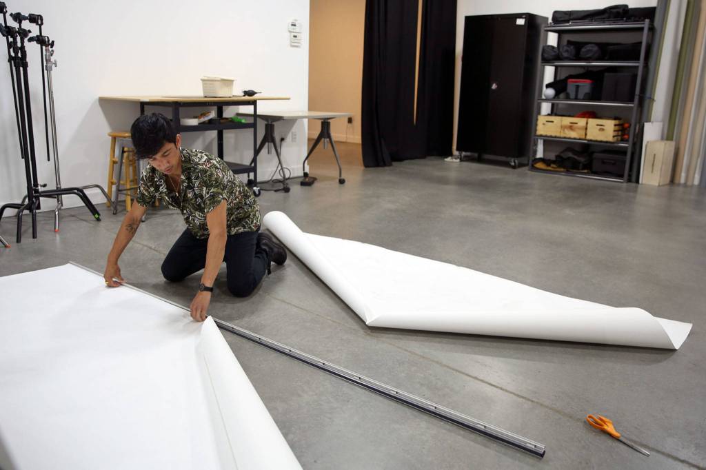 Mark Malijan adjust background paper at his for-rent photo-video studio in Edmonds. (Kevin Clark / The Herald)