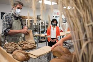 Dr. Stephen Jones, left, of the WSU Bread Lab, packages up loaves of bread for U.S. Trade Representative Katherine Tai, center, at the end of her tour of the Bread Lab at on Thursday, Aug. 5, 2021 in Burlington, Wash. (Olivia Vanni / The Herald)