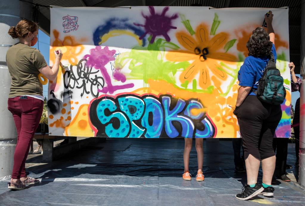 People add to a collective spray paint mural hosted by JAG Artworks on Sunday during the Delta Art Experience in Everett. (Olivia Vanni / The Herald)