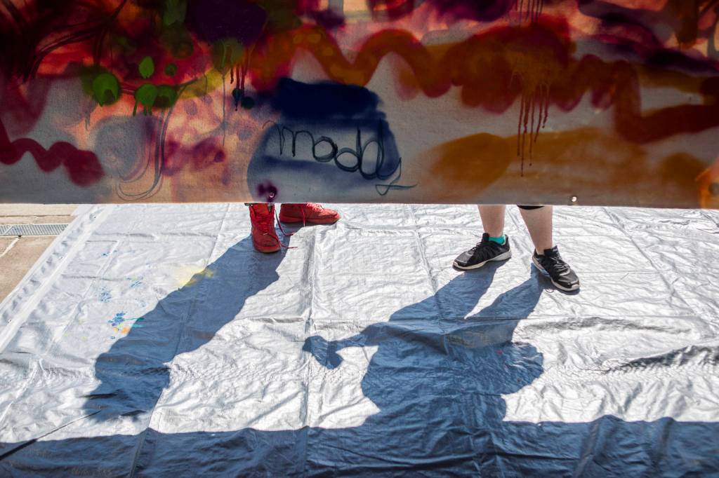 People spray paint on a mural hosted by JAG Artworks during the Delta Art Experience on Sunday in Everett. (Olivia Vanni / The Herald)
