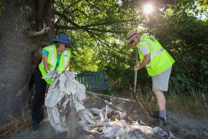 Lions Club treasurer Renee Deierling, left and Mike Edwards pull out plastic and netting to clear a space for one of two benches they installed at Pilchuck Park (Julia Landing) on Wednesday, Aug. 4, 2021 in Snohomish, Washington. The benches are the result of a recycling program, Bags-to-Benches, launched by the Snohomish Lions Club last November. The Lions and other local groups have been collecting recycled plastic to send to a company that, in turn, donates benches made from composite recycled materials. (Andy Bronson / The Herald)