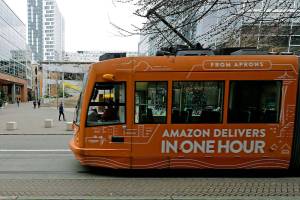FILE - This Nov. 13, 2018 file photo a South Lake Union streetcar with an advertisement for Amazon.com's same-day delivery service passes by an Amazon office building in Seattle's South Lake Union neighborhood. Amazon has pushed back its return-to-office date for tech and corporate workers until January 2022 as COVID-19 cases surge nationally due to the delta variant. The Seattle Times reported on the tech giant's delay in returning to offices from internal messages. (AP Photo/Ted S. Warren,File)