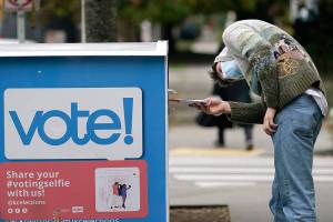 FILE - In this Oct. 28, 2020, file photo, a voter turns sideways as he eyes the opening of a ballot drop box before placing his ballot inside it in Seattle. A record number of voters participating in November's election was among Washington state's top stories for 2020. (AP Photo/Elaine Thompson, File)