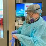 FILE - In this Aug. 20, 2021, file photo, two visitors peer into the room of a COVID-19 patient in the intensive care unit at Salem Hospital in Salem, Ore., as a nurse dons full protective gear before going into the room of another patient. Gov. Kate Brown announced Wednesday, Aug. 25, 2021, that the state has contracted with a medical staffing company to provide up to 500 health care workers to hospitals around the state to help respond to the surge in patients due to the delta variant. (AP Photo/Andrew Selsky, File)