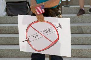 A sign that reads "No Jab" is held by a person taking part in a demonstration opposing mask and COVID-19 vaccine mandates outside the Legislative Building, Wednesday, Aug. 18, 2021, at the Capitol in Olympia, Wash. Washington Gov. Jay Inslee announced Wednesday that Washington state is expanding its vaccine mandate to include all public, charter and private school teachers and staff, as well as those working at the state's colleges and universities. Inslee also expanded the statewide indoor mask mandate in place for non-vaccinated individuals to include those who are vaccinated. (AP Photo/Ted S. Warren)