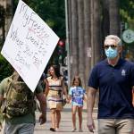A person toting a sign from a demonstration against mandatory vaccinations passes a man wearing a face mask by the Capitol in Sacramento, Calif. Across the country, anti-vaccine and anti-mask demonstrations are taking scary and violent turns, and educators, medical professionals and public figures have been stunned at the level at which they have been vilified for even stating their opinion. (Rich Pedroncelli / Associated Press file)
