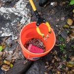 Needles are dropped into a bucket during an encampment cleanup Sunday east of I-5 between 128th Street SE and 130th Street SE near Everett. (Olivia Vanni / The Herald)