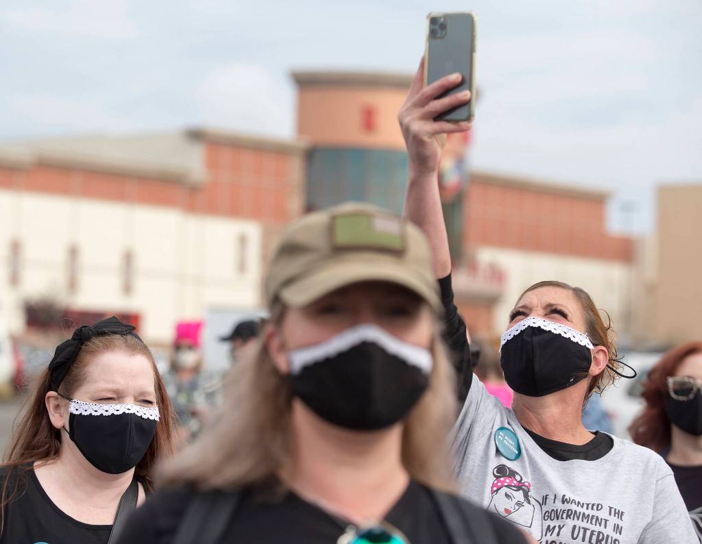 Wearing Ruth Bader Ginsburg masks, Christy Cheever (left) Janean Desmarais (center) and Carrie Caffrey hang out in the parking lot at the Everett Mall before marching with several hundred activists Saturday in support of reproductive rights in Everett. (Andy Bronson / The Herald)