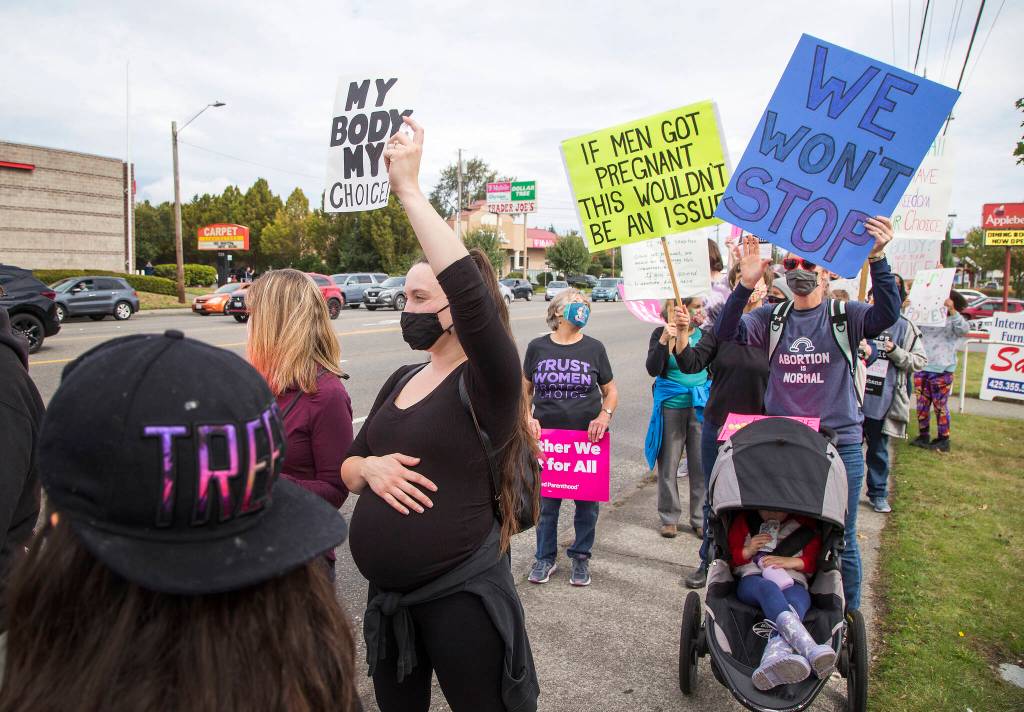 Visibly pregnant, Allison Stone holds up a sign and she and several hundred activists march in support of reproductive rights along Highway 99.on Saturday, Oct. 2, 2021 in Everett, Washington. (Andy Bronson / The Herald)