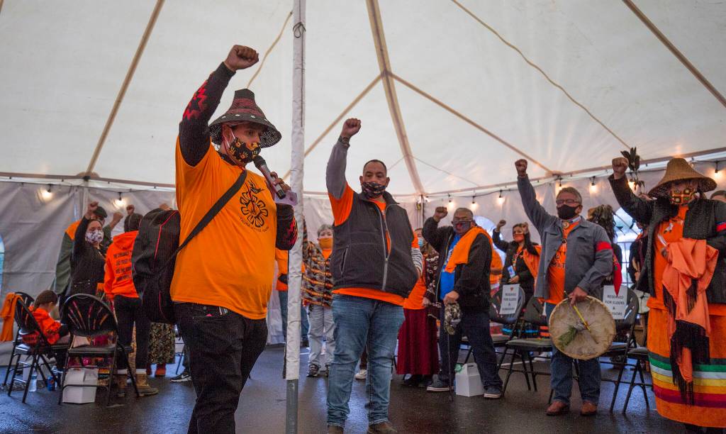 The Tulalip Tribes community members raise a fist as they gather at the last remaining building from the Tulalip Indian boarding school for a Day of Remembrance on Thursday in Tulalip Reservation. The Tulalip Tribes passed a resolution proclaiming Sept. 30 as Orange Shirt Day, a day of remembrance and awareness for Residential Boarding Schools. (Andy Bronson / The Herald)