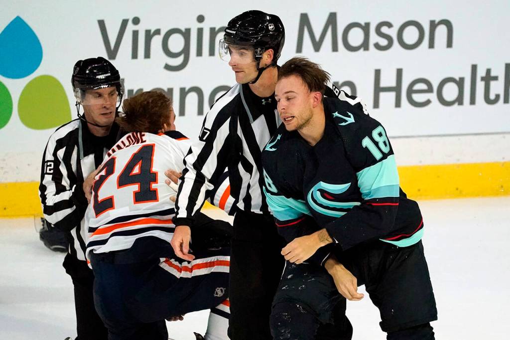 Seattle Krakens Carsen Twarysnki (18) is escorted off the ice as Edmonton Oilers Brad Malone (24) is assisted up after the two fought in the first period of a pre-season NHL hockey game Friday in Everett. (AP Photo/Elaine Thompson)