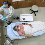 Angie Cleary, a registered nurse, cares for Joyce Johnson-Albert as she receives an antibody infusion while lying on a bed in a trauma room at the Upper Tanana Health Center Wednesday, Sept. 22, 2021, in Tok, Alaska. Johnson-Albert was optimistic but also realistic. "I just hope the next few days I'll be getting a little better than now," Johnson-Albert told a reporter on the other side of a closed, sliding glass door to the treatment room two days after testing positive for COVID-19 and while receiving an antibody infusion. "It's just hard to say. You can go either way." (AP Photo/Rick Bowmer)