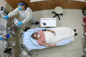 Angie Cleary, a registered nurse, cares for Joyce Johnson-Albert as she receives an antibody infusion while lying on a bed in a trauma room at the Upper Tanana Health Center Wednesday, Sept. 22, 2021, in Tok, Alaska. Johnson-Albert was optimistic but also realistic. "I just hope the next few days I'll be getting a little better than now," Johnson-Albert told a reporter on the other side of a closed, sliding glass door to the treatment room two days after testing positive for COVID-19 and while receiving an antibody infusion. "It's just hard to say. You can go either way." (AP Photo/Rick Bowmer)
