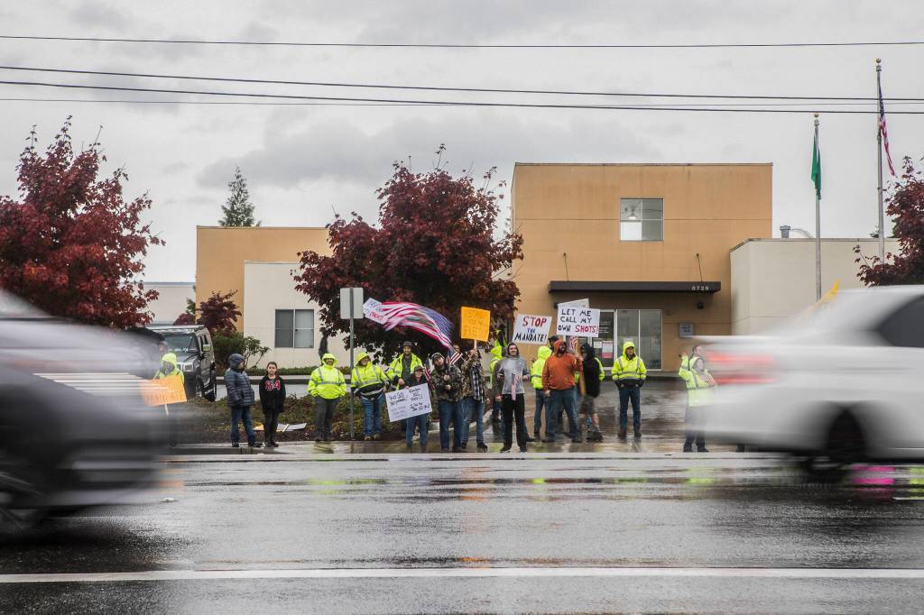 People hold signs in protest of the vaccine mandate along Airport Road next to Boeing on Friday in Everett. (Olivia Vanni / The Herald)