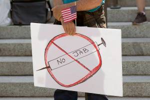 A sign that reads "No Jab" is held by a person taking part in a demonstration opposing mask and COVID-19 vaccine mandates outside the Legislative Building, Wednesday, Aug. 18, 2021, at the Capitol in Olympia, Wash. Washington Gov. Jay Inslee announced Wednesday that Washington state is expanding its vaccine mandate to include all public, charter and private school teachers and staff, as well as those working at the state's colleges and universities. Inslee also expanded the statewide indoor mask mandate in place for non-vaccinated individuals to include those who are vaccinated. (AP Photo/Ted S. Warren)