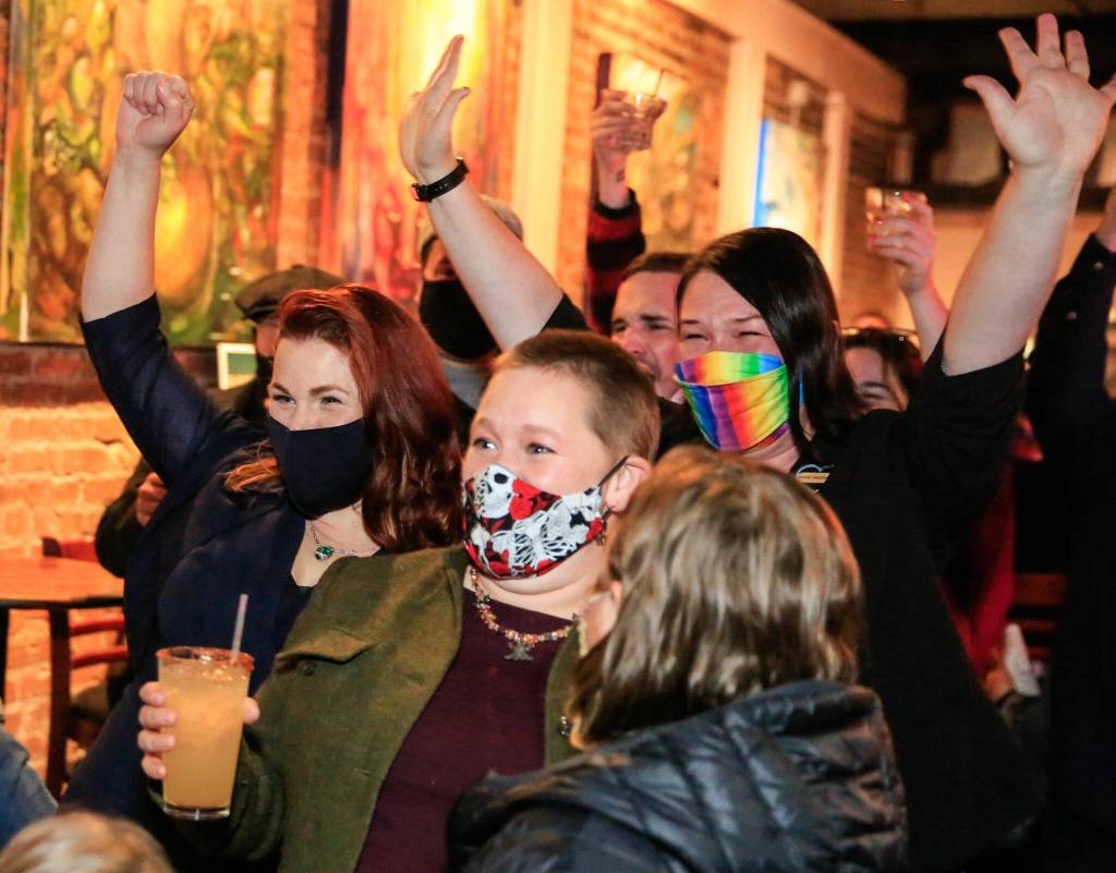 Mary Fosse (left), Liz Vogeli (center) and Paula Rhyne celebrate as election results are read aloud Tuesday night at Black Lab Gallery in Everett. (Kevin Clark / The Herald)