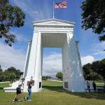 People walk adjacent to the border with Canada at the Peace Arch in Peace Arch Historical State Park, where cars behind wait to enter Canada at the border crossing Monday, Aug. 9, 2021, in Blaine, Wash. Canada lifted its prohibition on Americans crossing the border to shop, vacation or visit, but America kept similar restrictions in place, part of a bumpy return to normalcy from coronavirus travel bans. (AP Photo/Elaine Thompson)