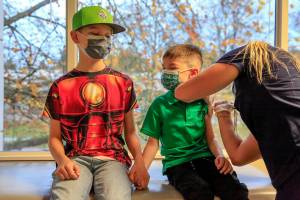 Gage Peterson, 11, holds Duke Peterson's, 6,  hand as he gets his COVID vaccination Saturday morning at North Sound Pediatrics in Mill Creek on November 6, 2021. (Kevin Clark / The Herald)
