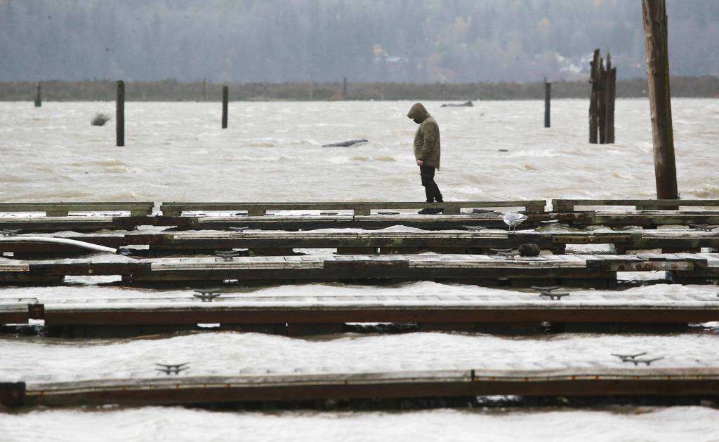 As waves and wind batter the floating docks, a man walks out on one at the 10th Street Boat Launch on Monday, Nov. 15, 2021 in Everett, Washington. (Andy Bronson / The Herald)