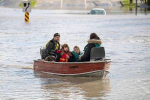 A woman and children who were stranded by high water due to flooding are rescued by a volunteer operating a boat in Abbotsford, British Columbia on Tuesday, Nov. 16, 2021. Officials in a small city near the Canada border are calling the damage devastating after a storm that dumped rain for days caused flooding and mudslides. City officials in Sumas, Washington said Tuesday that hundreds of people had been evacuated and estimated that 75% of homes had water damage. Just over the border, residents in about 1,100 rural homes in Abbotsford were told to evacuate as waterways started to rise quickly. (Darryl Dyck/The Canadian Press via AP)