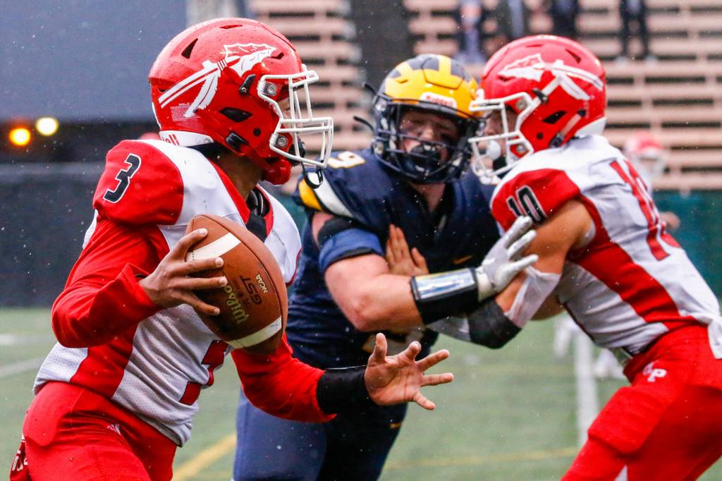 Marysville-Pilchucks Gaylan Gray looks to pass with Bellevues Casper Rublowsky closing with Marysville-Pilchucks Jordan Velasquez blocking Saturday afternoon at Memorial Stadium in Seattle on November 27, 2021. The Tomahawks fell to the Wolverines 27-3 ending their playoff run. (Kevin Clark / The Herald)
