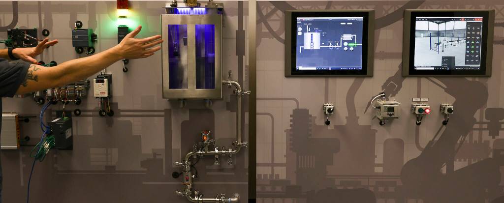 Everett Community Colleges Dennis Skarr sits in front of a 15-foot interactive wall that can replicate a manufacturing companys assembly line, hardware, software and networks. (Andy Bronson / The Herald)