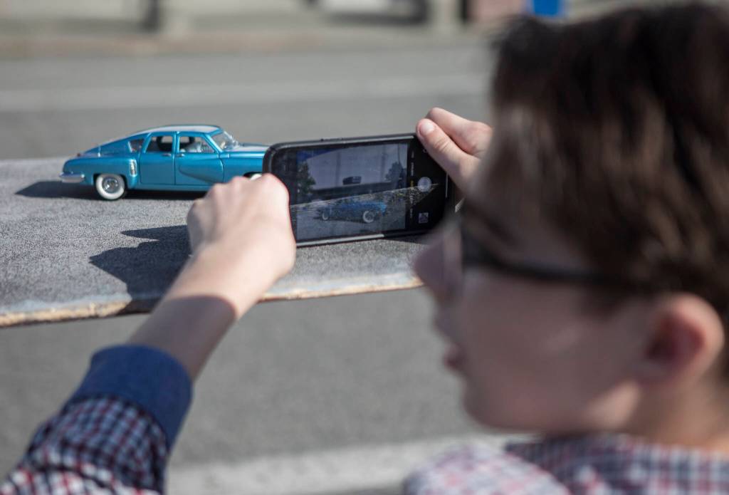 Anthony Schmidt uses his iPhone to take photographs of a model car in front of Everett High School. (Olivia Vanni / The Herald)