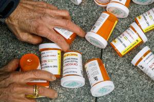 FILE - A protester gathers containers that look like OxyContin bottles at an anti-opioid demonstration in front of the U.S. Department of Health and Human Services headquarters in Washington, on April 5, 2019. A judge has kept lawsuits against OxyContin maker Purdue Pharma and members of the Sackler family who own it on hold until Feb. 1, 2022, but ordered the parties involved to negotiate a new settlement. (AP Photo/Patrick Semansky, File)