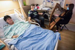 Shelly Holmgren, left, holds hands with her brother Jay Holmgren, center, while they listen to Musicial Thanatologist April Mitchell a song at Providence Everett on Friday, Dec. 17, 2021 in Everett, Wa. (Olivia Vanni / The Herald)