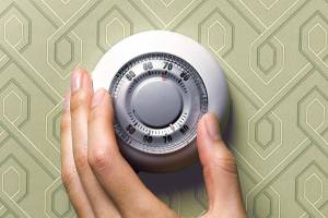 Woman adjusting thermostat on green wallpapered wall, close-up