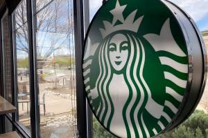 A sign bearing the corporate logo hangs in the window of a Starbucks open only to take-away customers in this photograph taken Monday, April 26, 2021, in southeast Denver.  Starbucks is no longer requiring its U.S. workers to be vaccinated against COVID-19, reversing a policy it announced earlier this month. The Seattle coffee giant says, Wednesday, Jan. 19, 2022,  it's responding to last week’s ruling by the U.S. Supreme Court.  (AP Photo/David Zalubowski)