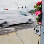 A car drives by flowers placed at a memorial for two pedestrians killed at the corner of 204th Street NE and Highway 9 on Friday, Jan. 21, 2022 in Arlington, Washington. (Olivia Vanni / The Herald)