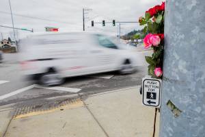A car drives by flowers placed at a memorial for two pedestrians killed at the corner of 204th Street NE and Highway 9 on Friday, Jan. 21, 2022 in Arlington, Washington. (Olivia Vanni / The Herald)