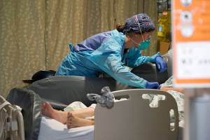 Registered nurse Estella Wilmarth tends to a patient in the acute care unit of Harborview Medical Center, Friday, Jan. 14, 2022, in Seattle. Washington Gov. Jay Inslee is deploying 100 members of the state National Guard to hospitals across the state amid staff shortages due to an omicron-fueled spike in COVID-19 hospitalizations. Inslee announced Thursday that teams will be deployed to assist four overcrowded emergency departments at hospitals in Everett, Yakima, Wenatchee and Spokane, and that testing teams will be based at hospitals in Olympia, Richland, Seattle and Tacoma. (AP Photo/Elaine Thompson)