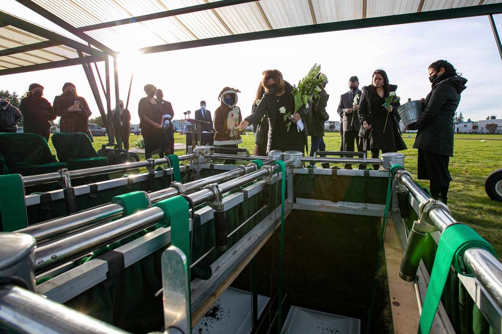 Grandmother Irma Amundson tosses soil onto the graves of her granddaughters, Adriana and Mariel Gil, during the girls funeral Friday, Jan. 28, 2022, at Cypress Lawn Memorial Park in Everett. (Ryan Berry / The Herald)